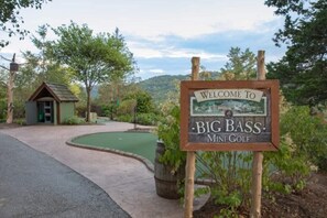 A welcome sign for Big Bass Mini-Golf with a small building in the background. - Big Cedar | Rustic Retreat | Pools, Lake & Adventure (Ridgedale)