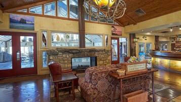 A spacious lobby with a stone fireplace, wooden ceiling, and a large window overlooking the outside.