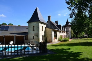 Ein Steinhaus mit Schwimmbad, einer überdachten Terrasse und einem Turm.
