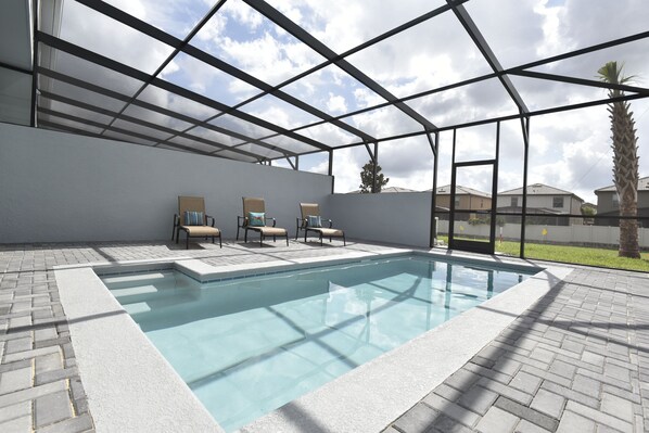 A swimming pool with a glass ceiling, surrounded by lounge chairs and a brick patio.