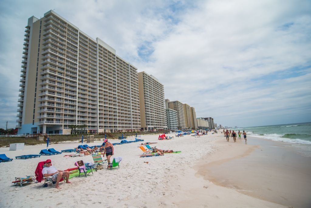 A beach with rows of beach chairs and umbrellas, a sandy shore, and tall buildings in the background.