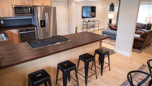 Een moderne keuken met een centraal eiland, barstoelen, een magnetron, een koelkast en een eethoek met een televisie en zitplaatsen.
