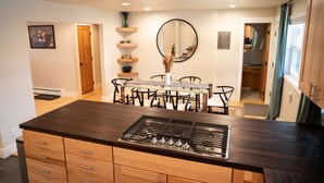 Een moderne keuken met een centraal eiland, een eethoek met een glazen tafel en stoelen, en een grote spiegel aan de muur.
