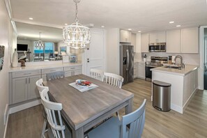 A modern kitchen with white cabinets, stainless steel appliances, and a wooden dining table with chairs. - Oceanview from every room! Corner Condo lots of windows! - E112 North Coast Village (Oceanside)