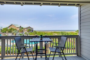 A balcony with a table and two chairs, overlooking a swimming pool and beachfront houses. - St Helena Island Condo - 1/2 Mi to Beach (Saint Helena Island)