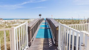 A wooden boardwalk leading to a beach with a blue mat on the path.