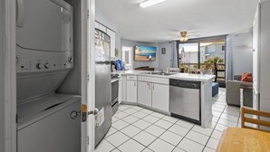 A modern kitchen with a built-in washer and dryer, a large island with a sink, and a view of the beach through the window.