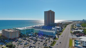 A hotel with a parking lot, a beach view, and a tall building in the background.