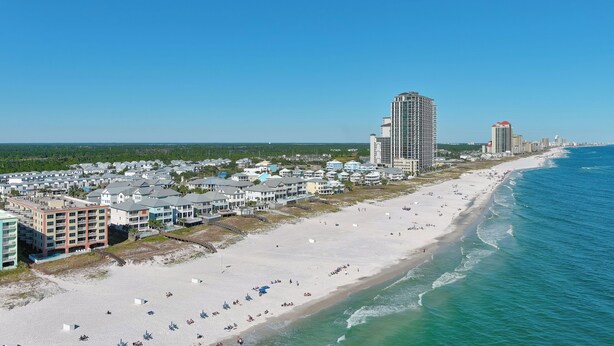 A coastal cityscape with a beach, high-rise buildings, and a clear blue sky.