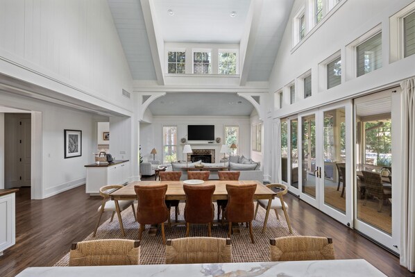 A spacious dining area with a large wooden table and six chairs, a fireplace, and a view through glass doors to an outdoor patio.