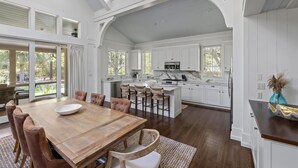 Een ruime keuken met witte kasten, een groot eiland en een eetgedeelte met een houten tafel en stoelen.