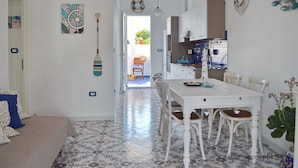 Une cuisine avec des meubles blancs, une table à manger avec des chaises et une vue sur l’extérieur.