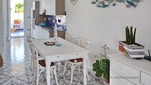 Une cuisine avec des meubles blancs, un pare-feu en carreaux et un coin repas comprenant une table et des chaises blanches.