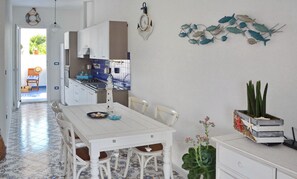 A kitchen with white cabinets, a tiled backsplash, and a dining area with a white table and chairs.