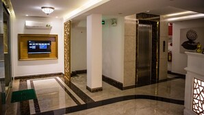 Eine moderne Hotelhalle mit Digitalanzeige, Aufzug und einem gemusterten Boden.