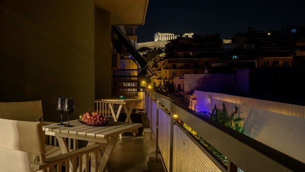 A balcony with a table, two wine glasses, and a bowl of grapes. - Acropolis Grand Apartment (Athina)