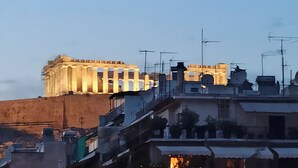 A classical building with columns and a large archway, surrounded by modern buildings with visible antennas. - Acropolis Grand Apartment (Athina)