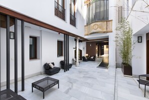 A spacious courtyard with a modern outdoor seating area, a large potted plant, and a view of the interior through an open doorway. - Elvira Suites (Granada)