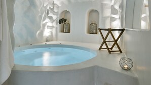 Un baño moderno con una bañera grande, un taburete de madera y apliques decorativos en la pared.