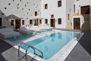 Un área de piscina moderna al aire libre, con una piscina cristalina, sillas de descanso blancas y sombrillas.
