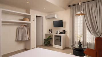 Habitación de hotel con cama, zona de estar con una silla, televisor montado en la pared, una mesita con un florero y una planta.