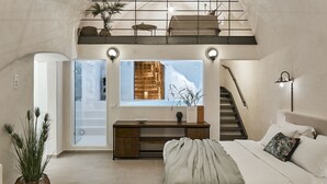 Un espacioso dormitorio tipo loft con techo alto, cama grande, escritorio y escalera que conduce a un nivel superior.