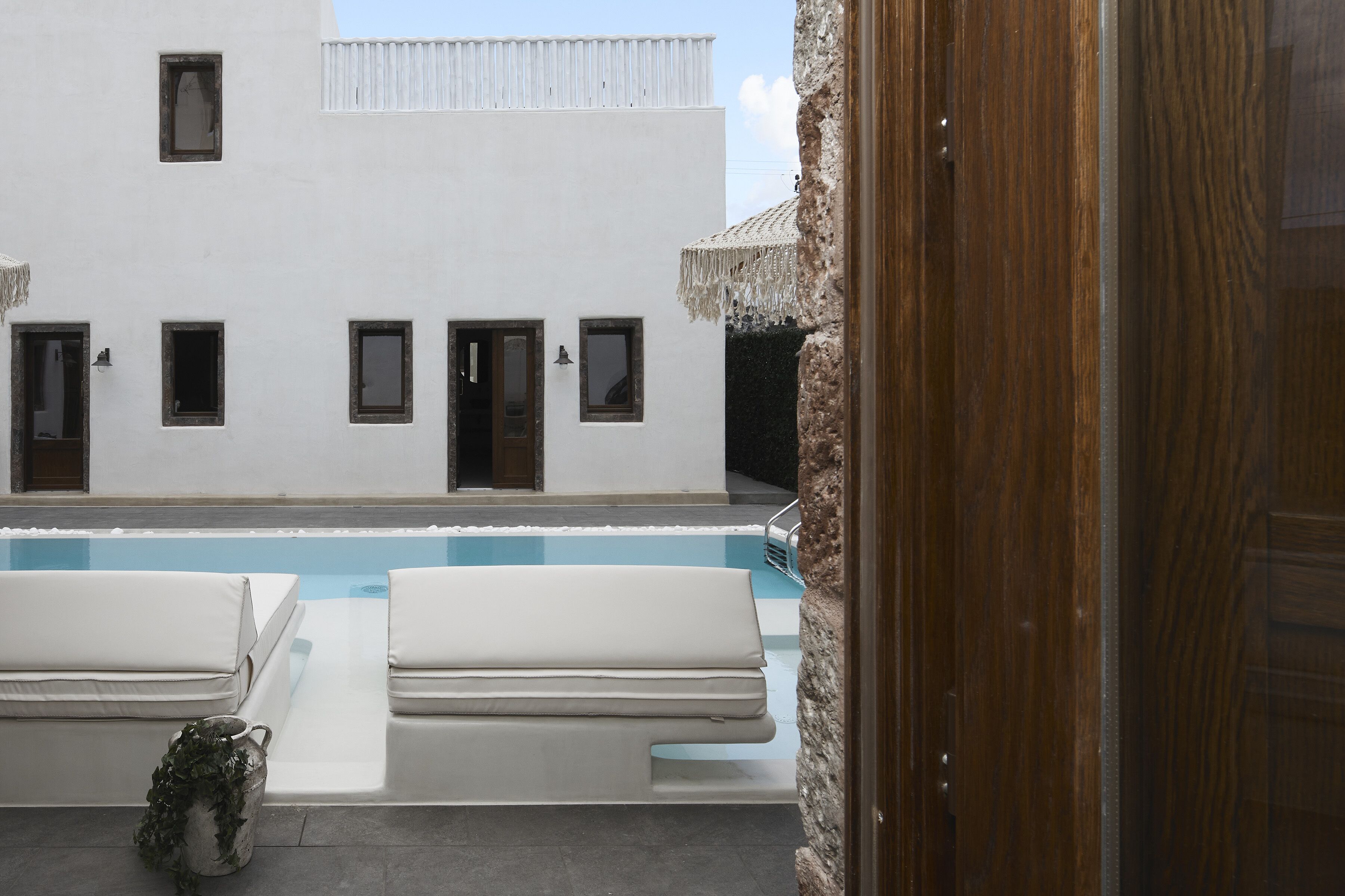 A pool area with two white lounge chairs, a clear blue pool, and a white building with multiple windows.