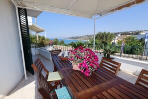 A wooden table with chairs and a potted plant with pink flowers on a balcony with a view of the sea. - BEACH HOUSE WITH A VIEW OF THE SEA (Patù)