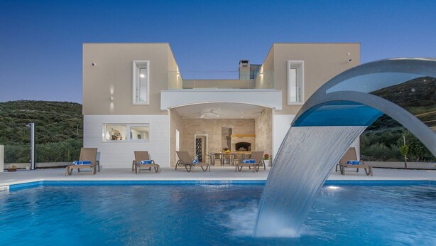 Een modern huis met een zwembad, een waterval en een eethoek.