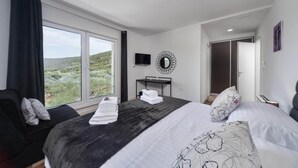 Een slaapkamer met een groot bed, een bureau, een televisie en uitzicht op een natuurlandschap.