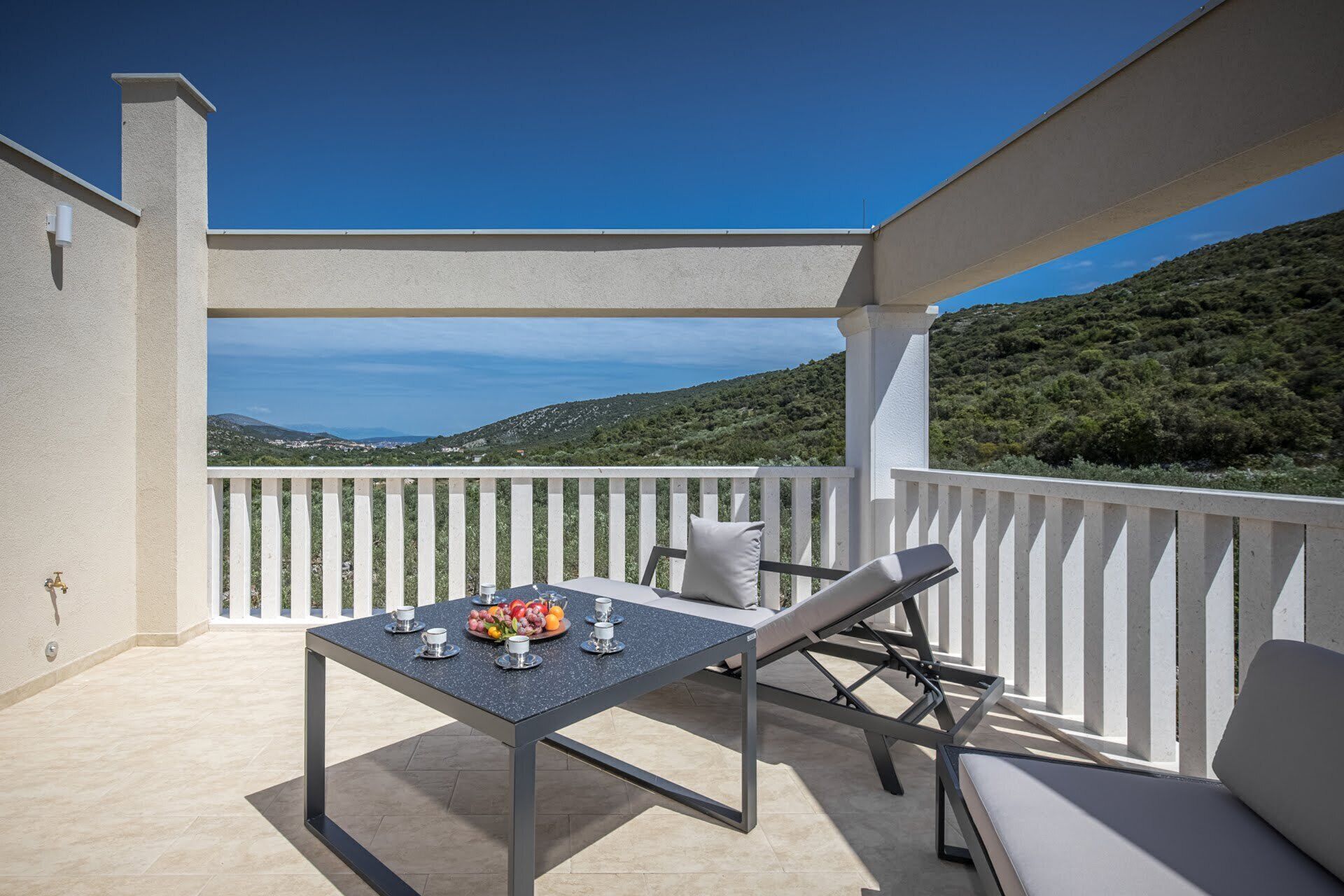 Un balcon avec une table dressée pour deux personnes, une balustrade blanche et une vue sur un paysage vallonné.