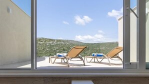 Een balkon met twee loungestoelen en een trap van betonblokken naar een terras.