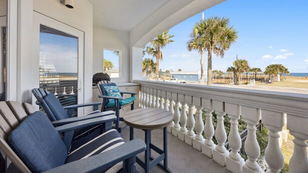 A balcony with a view of the beach, featuring a seating area with chairs and a table.