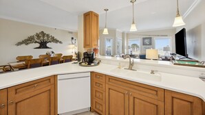 A modern kitchen with a large island, wooden cabinets, pendant lights, and a decorative tree wall art piece.