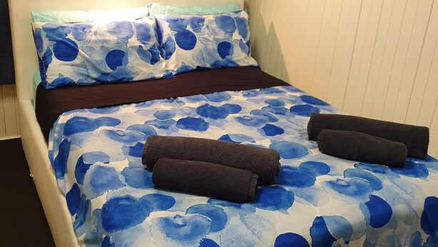 A bed with a blue and white floral bedspread, two dark brown towels, and a light-colored headboard. - Meyenburg Unit 4, 1 Double Beds, 1 Single 3 pax (Mount Morgan)