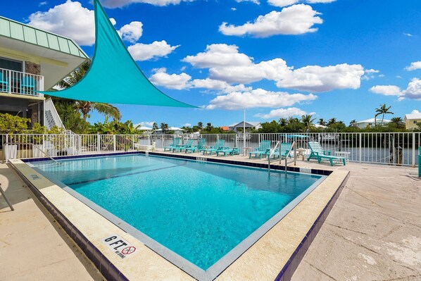 A rectangular swimming pool with a clear blue water surface, surrounded by a white fence and several turquoise lounge chairs.