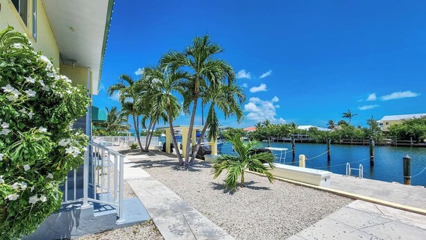 A waterfront property with a pool, palm trees, and a clear blue sky. - Fishing Till Sunset 1bed/1bath Condo w/Pool & dock (Marathon)