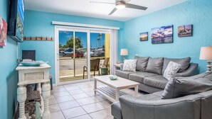 A living room with a grey sofa, a coffee table, a TV, and a ceiling fan. - Fishing Till Sunset 1bed/1bath Condo w/Pool & dock (Marathon)