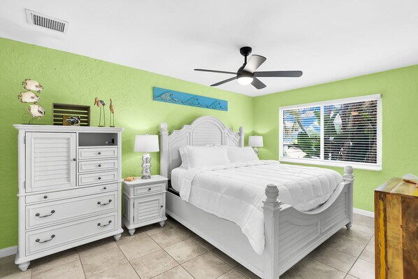 A bedroom with a bed, nightstands, a dresser, a ceiling fan, and a window with blinds.
