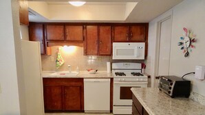 Une cuisine compacte dotée de meubles en bois, d’un four à micro-ondes, d’une cuisinière, d’un lave-vaisselle et d’un grille-pain.
