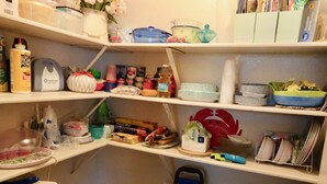 Une cuisine avec des étagères remplies de divers produits alimentaires et ustensiles de cuisine, ainsi qu’une valise bleue.