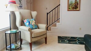 Un salon avec un fauteuil beige, une lampe sur pied, une petite table avec un livre et un escalier.