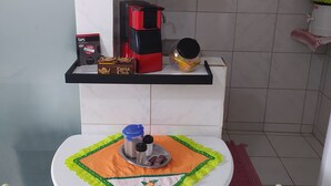 Eine kleine Küchenzeile mit einer Kaffeemaschine, einem Regal mit Küchenutensilien und einem Tisch mit Unterlage.