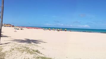 Uma praia com palmeiras, guarda-sóis e céu claro.
