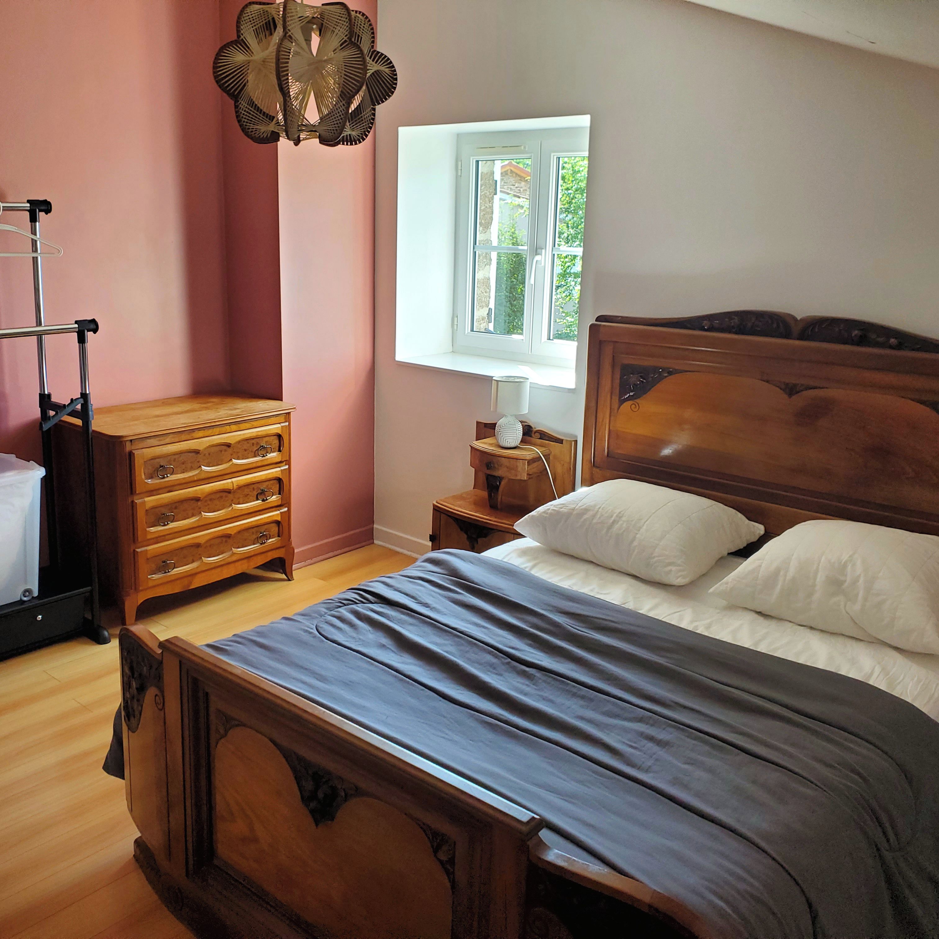 Une chambre à coucher avec un lit en bois, une table de chevet avec une lampe, une commode et une fenêtre donnant sur un paysage verdoyant.