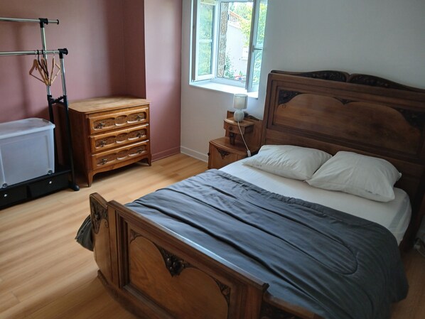A bedroom with a wooden bed, a dresser, a radiator, and a window with a view of greenery.