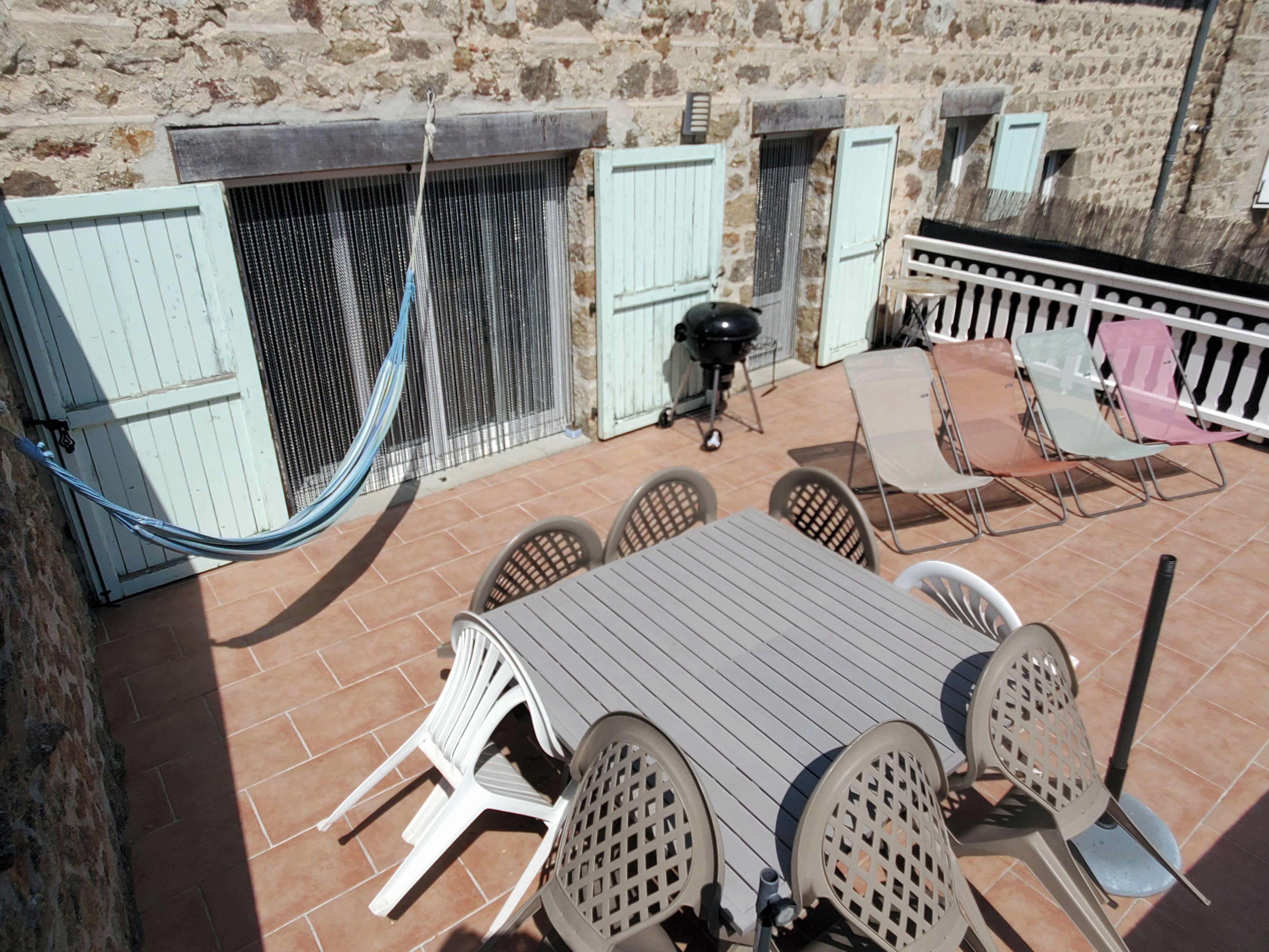 Une terrasse extérieure avec une table et des chaises, un hamac et un barbecue.