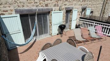 Une terrasse extérieure avec une table et des chaises, un hamac et un barbecue.