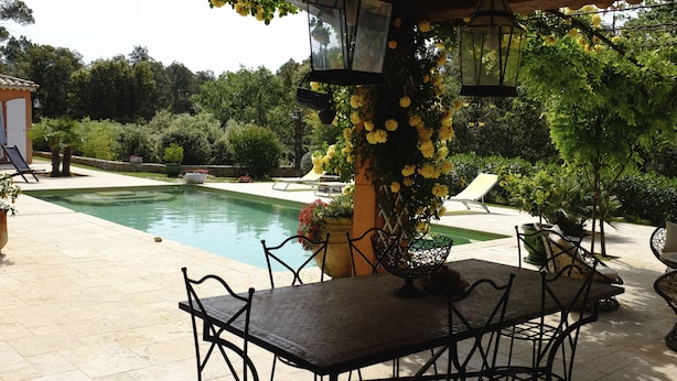 A poolside area with a table and chairs, surrounded by lush greenery and yellow flowers. - ABSOLUTE QUIET 45 km from the sea (St-Maxime St-Tropez). (Lorgues)