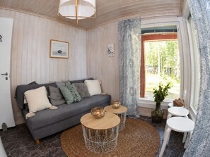 A cozy living room with a grey sofa, two small round tables, and a large window with curtains. - Seaside Villa with jacuzzi and own beach (Maksamaa (Vöyri))